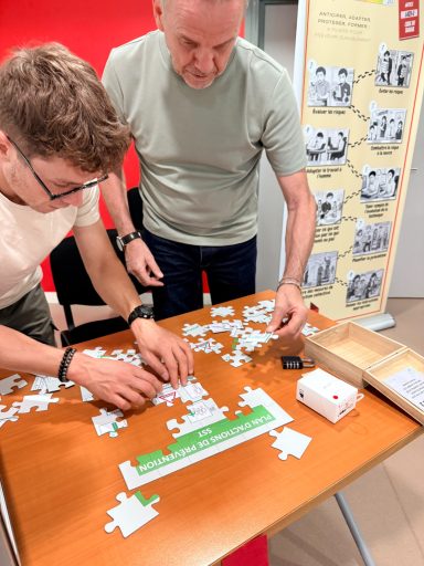 Le PAP en puzzle Deux personnes assemblent un puzzle sur une table en bois avec des pièces éparpillées.